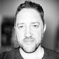 Black and white picture of a man with a light beard, short hair, and a t-shirt.